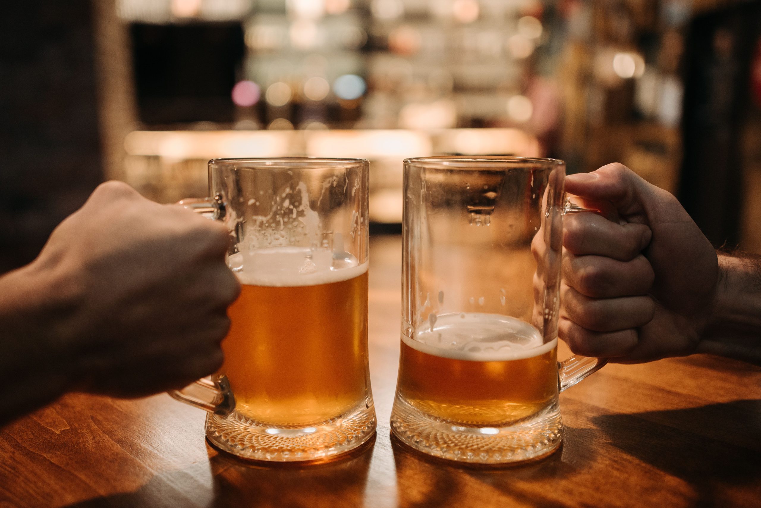 Foto de duas mãos segurando canecas de cerveja com cerveja clara dentro