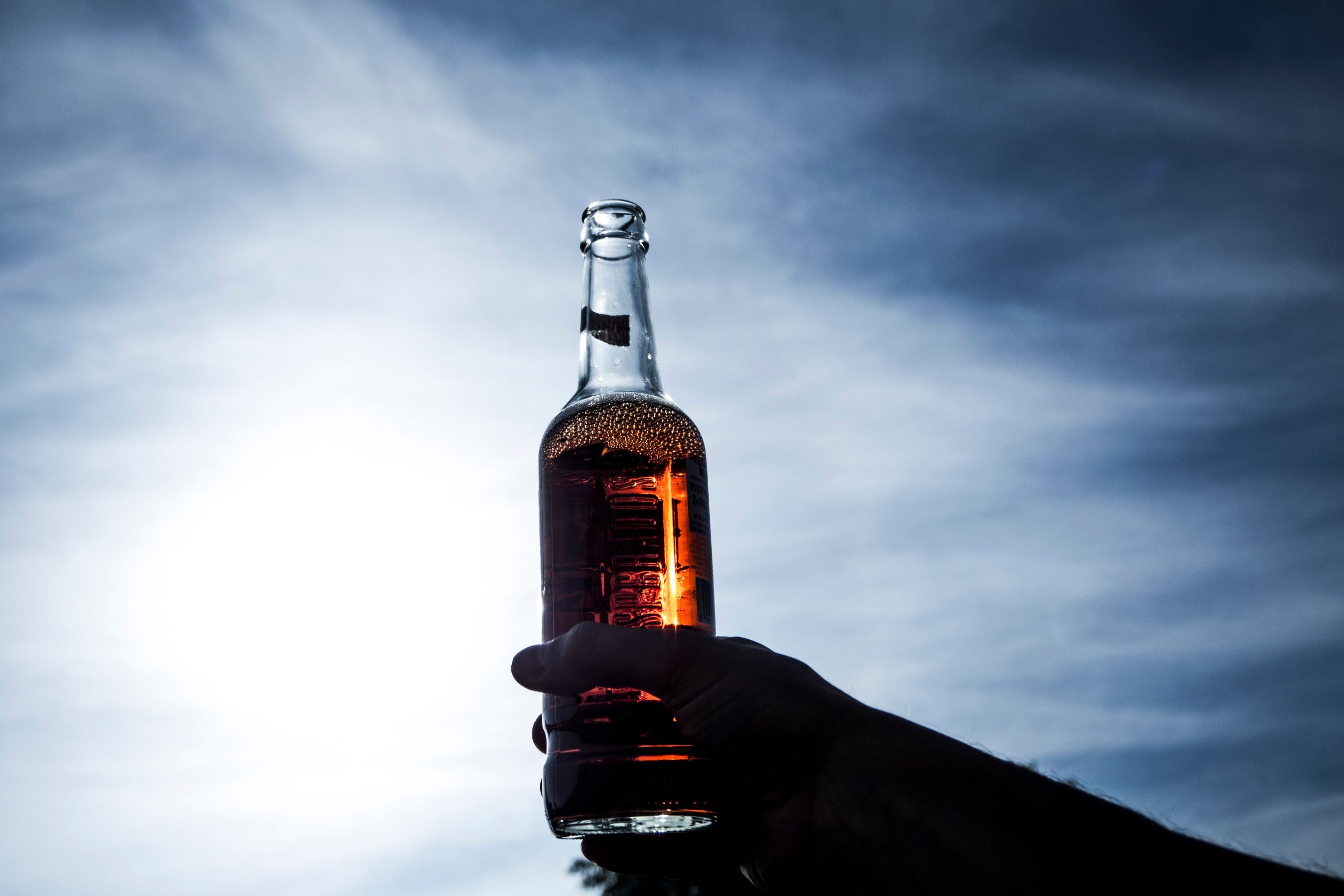 Mão segurando uma garrafa de cerveja, no fundo, o céu