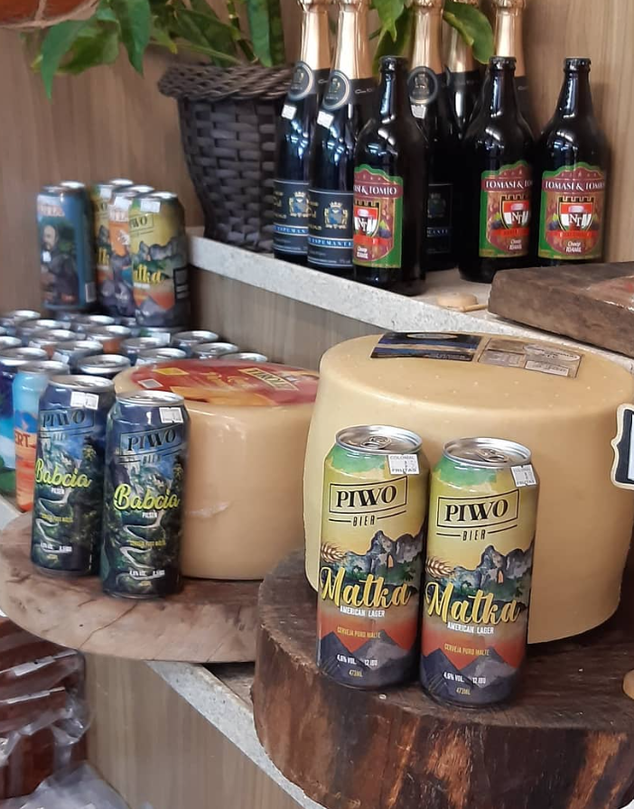 Foto de latas da cerveja Piwo ao lado de queijos e demais quitutes