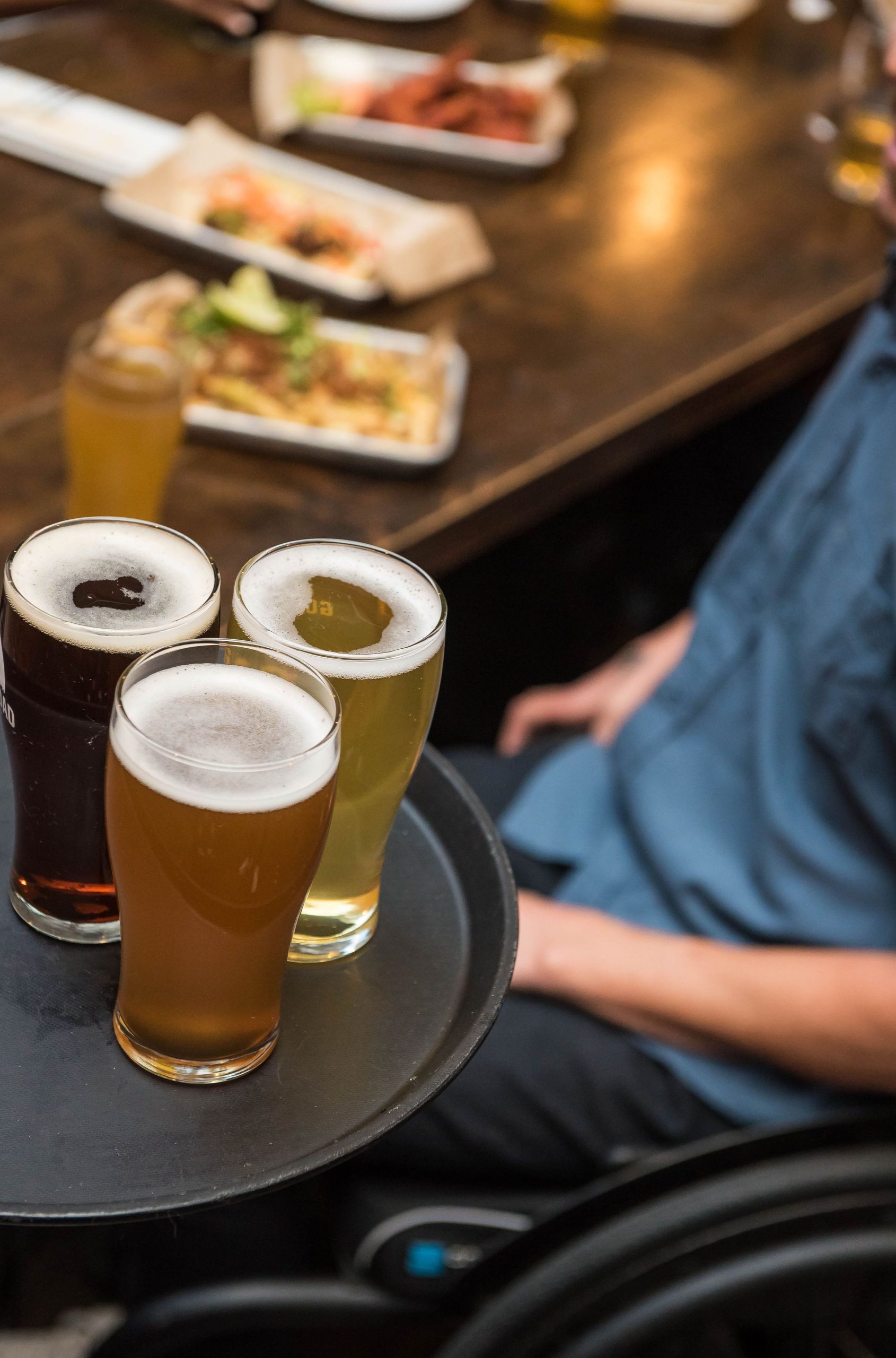 Foto de uma mesa com quitutes e em foco está uma badeja com vários pints de chope