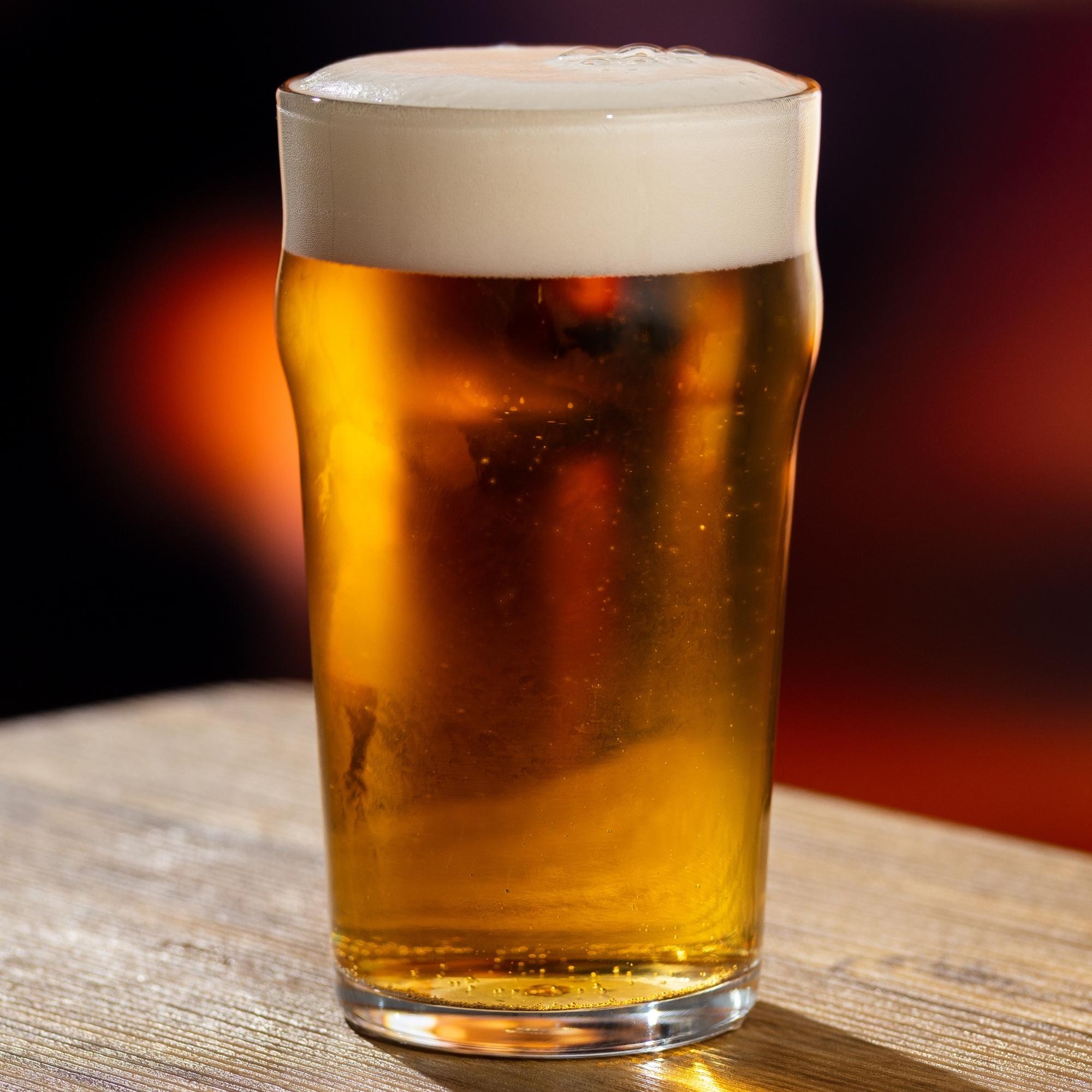 foto de um pint nonick com cerveja sobre mesa de madeira