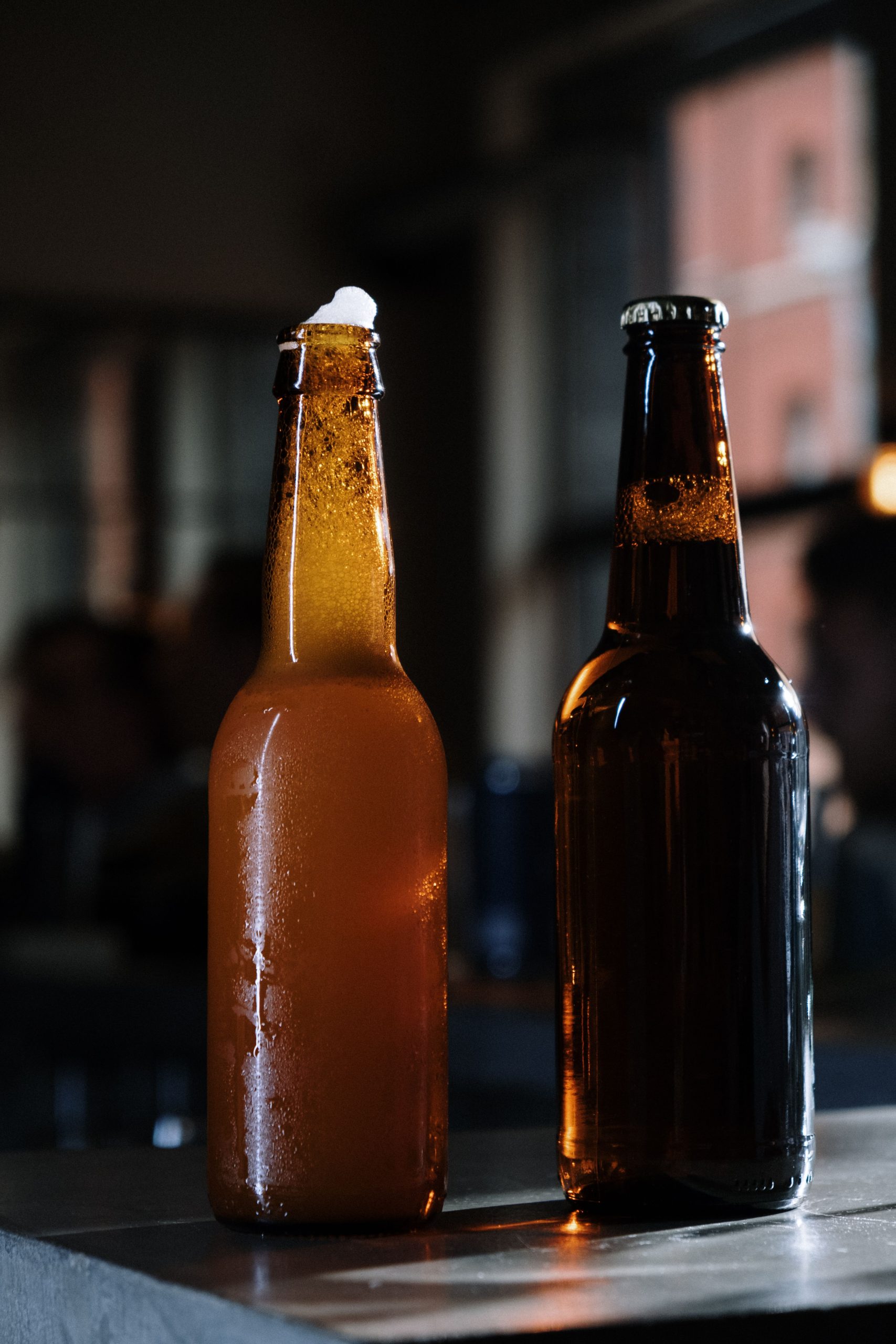 foto de duas garrafas de cerveja, uma aberta mostrando a espuma saindo e outra fechada