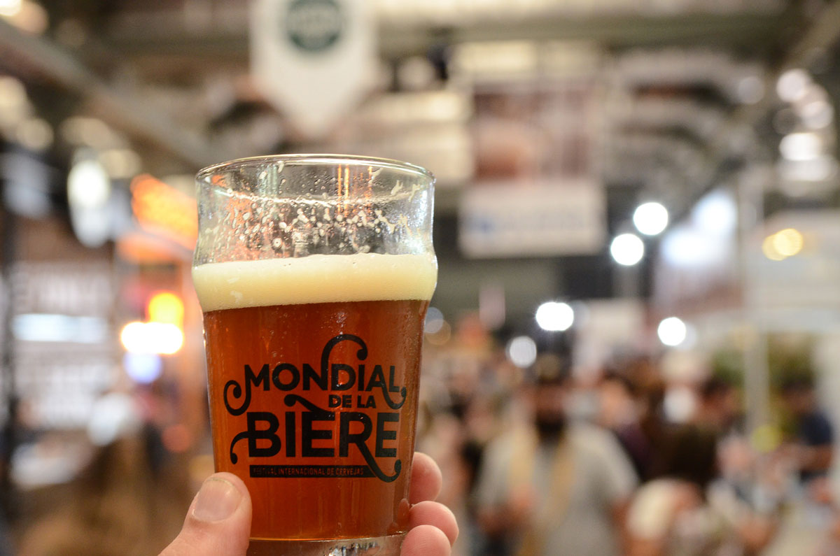 pessoa segurando um pint com o nome do evento e, ao fundo, várias pessoas andando