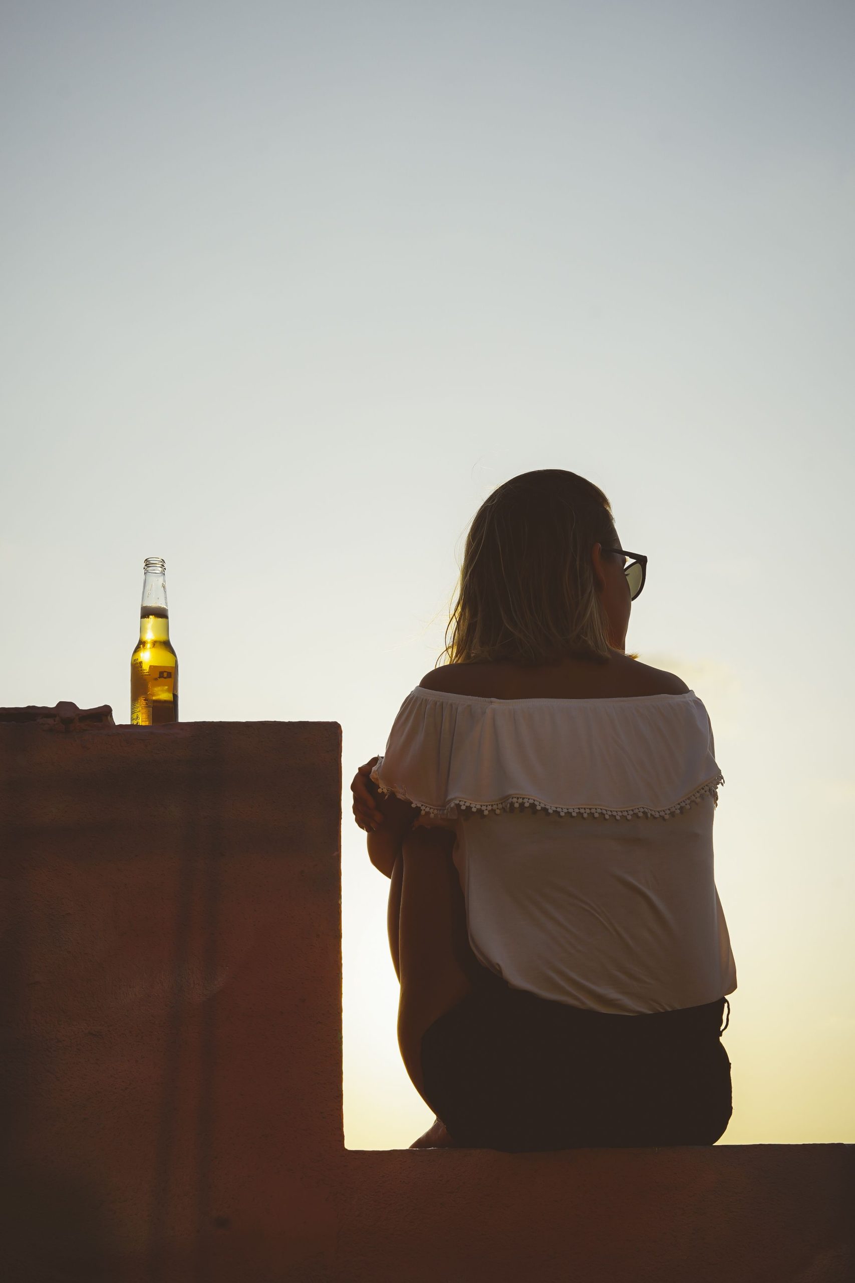 Mulher bebe cerveja enquanto olha o por do sol