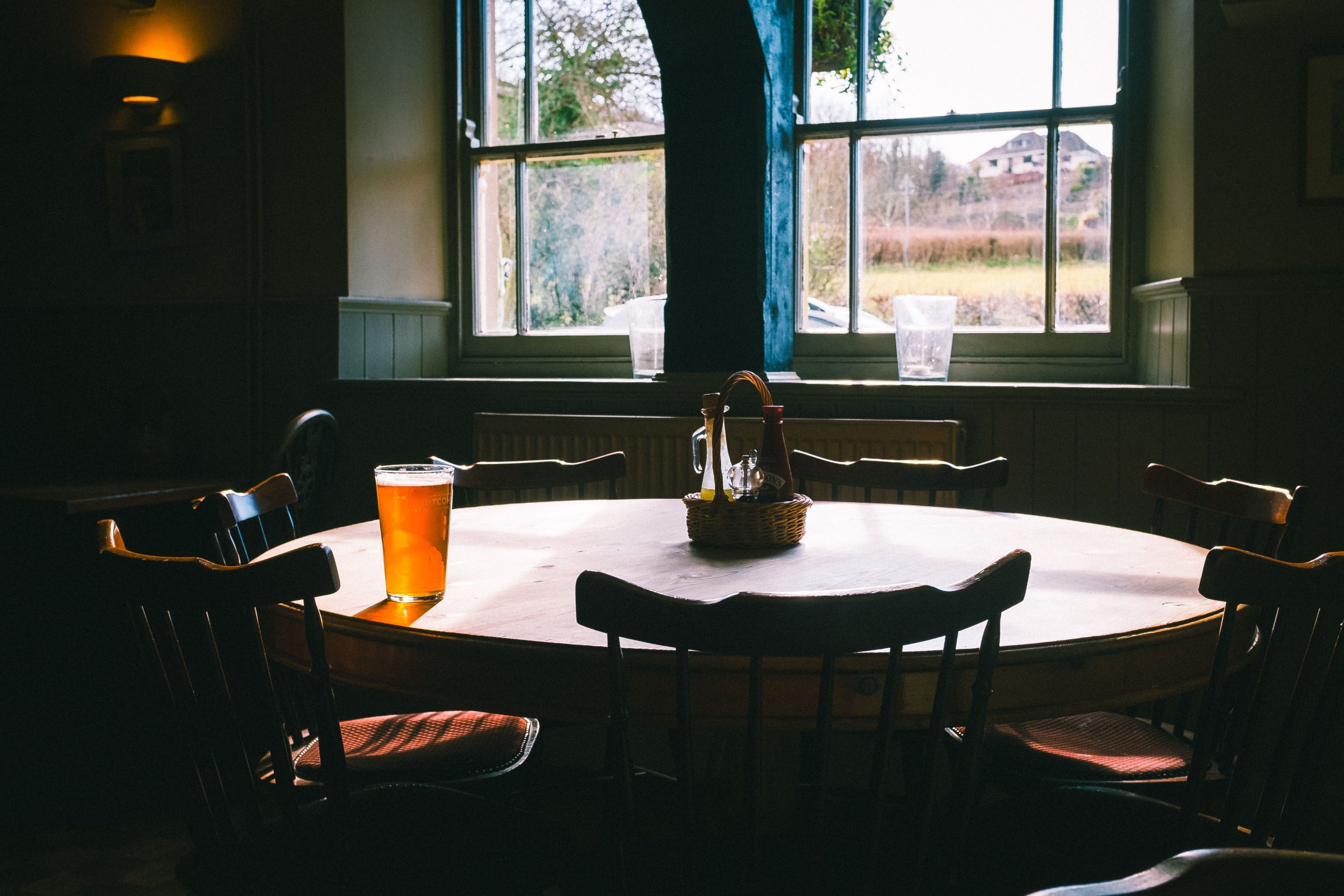 foto de mesa redonda de madeira, com cadeiras em volta, e uma unica cerveja no meio